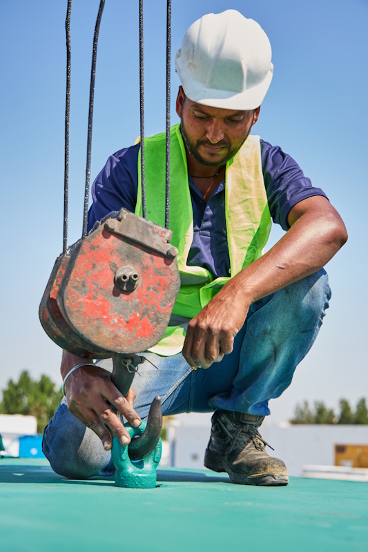 Certified rigger attaching heavy-duty crane hook to equipment canopy